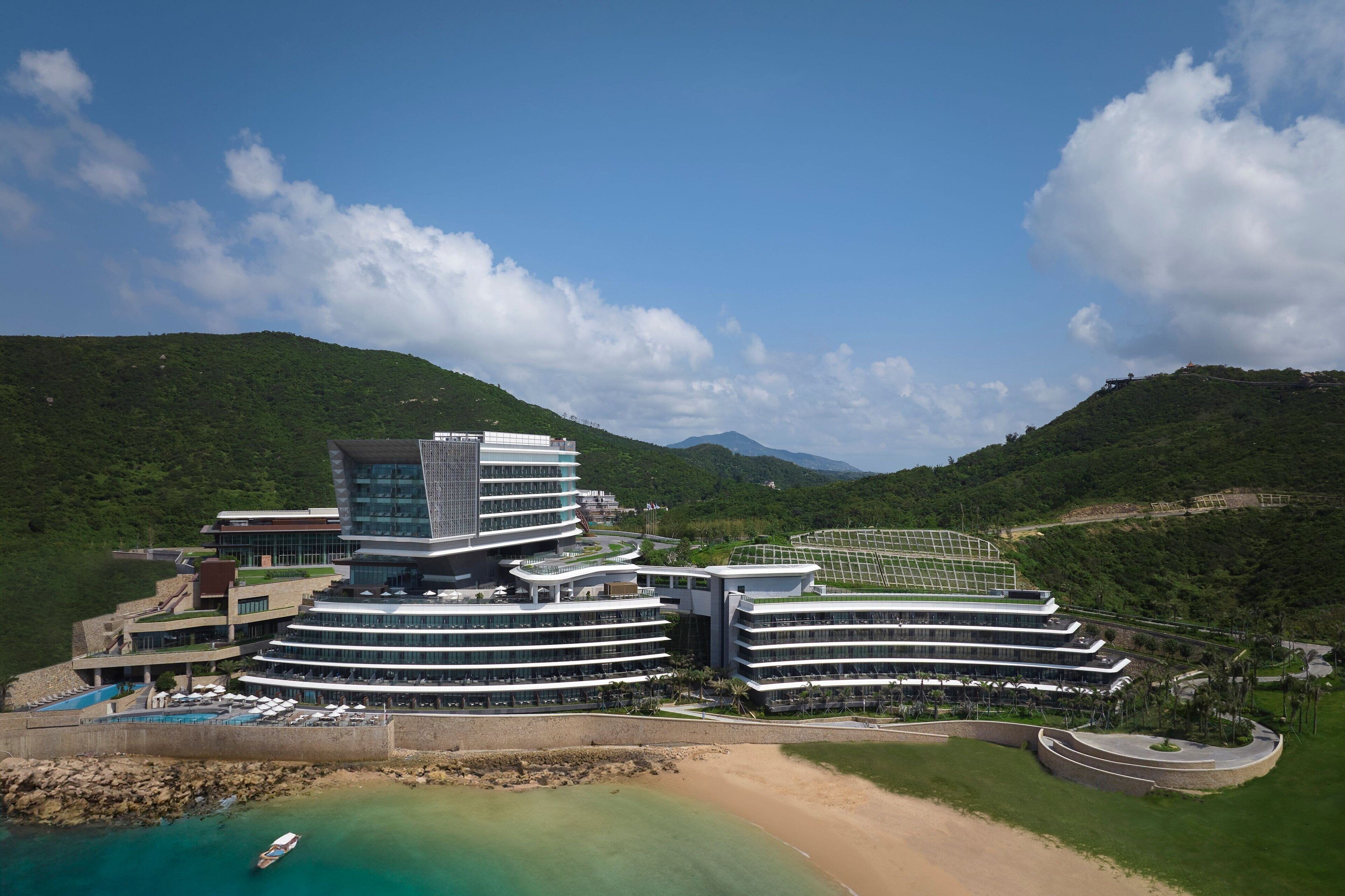 Un hotel moderno con un diseño circular único, situado cerca de una playa con aguas turquesas cristalinas.