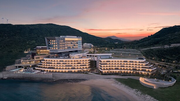 Un hotel moderno con varias edificaciones, una playa y un paisaje montañoso.
