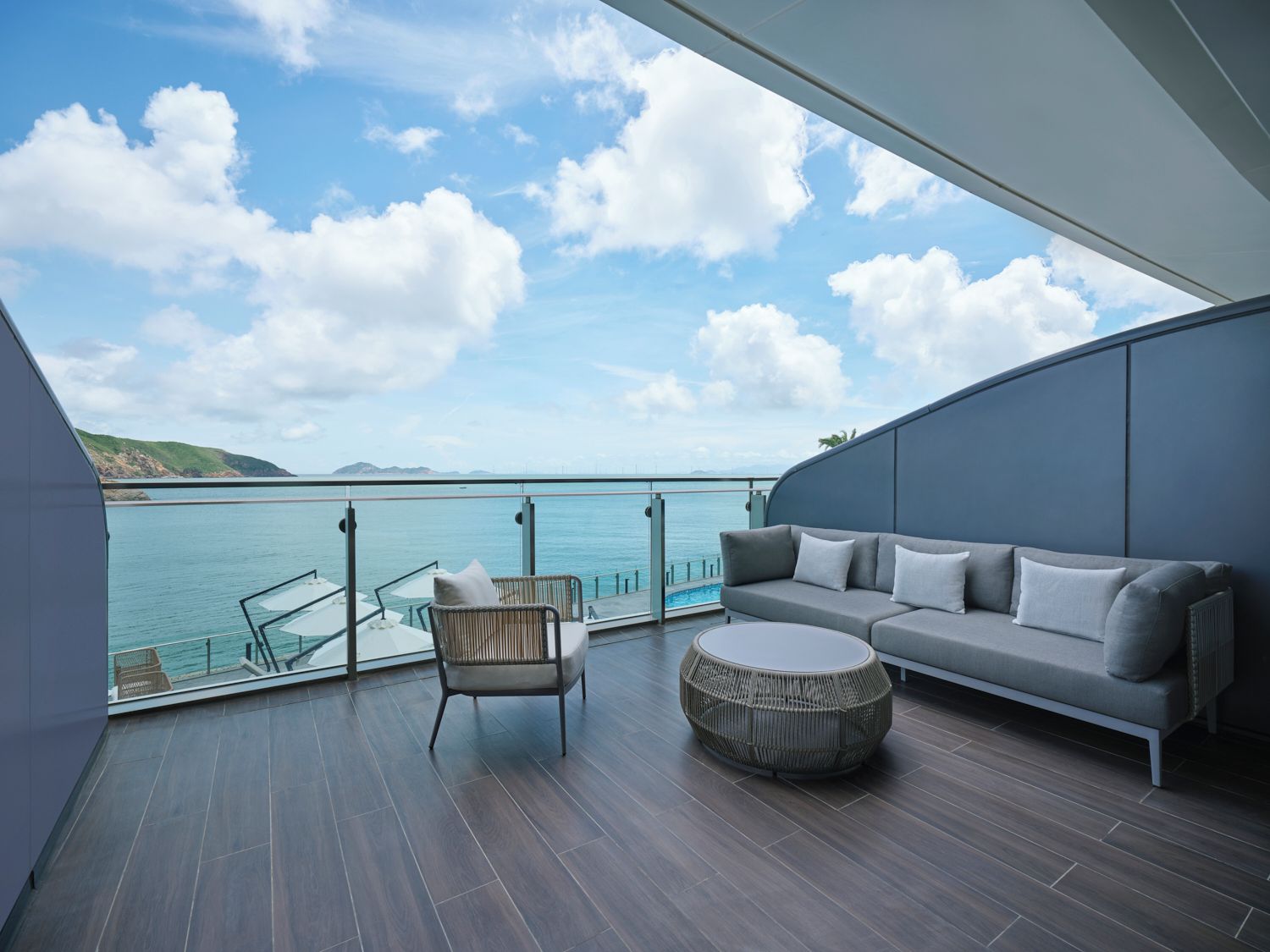 A balcony with a sofa, chair, and round table, overlooking a body of water and distant land.