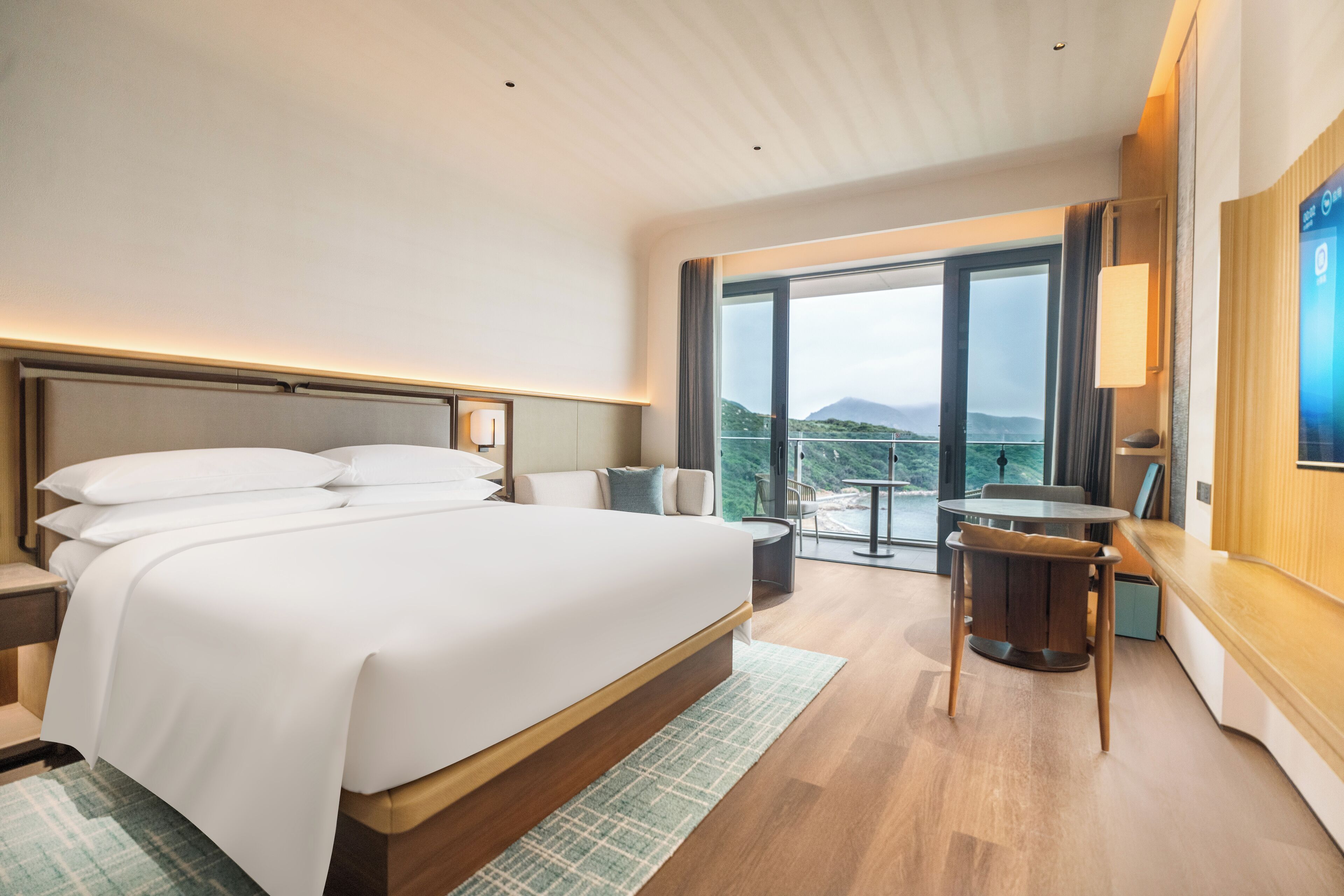 Une chambre d’hôtel moderne avec un grand lit, une petite table et un balcon offrant une vue sur les montagnes.