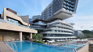Un hotel moderno con un diseño arquitectónico único, que cuenta con una zona de piscina con sillones reclinables y sombrillas.