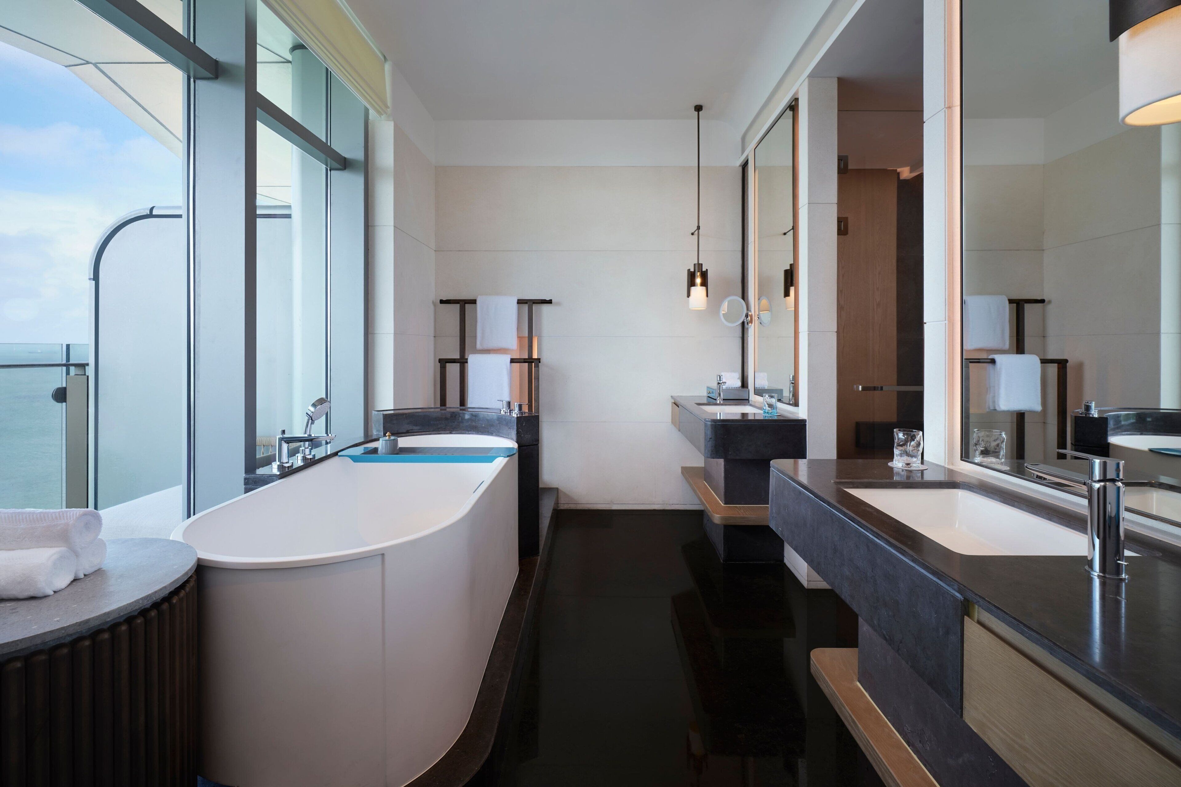 A modern bathroom with a freestanding bathtub, two sinks, and large mirrors.