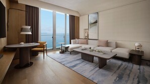 Una habitación de hotel moderna con un ventanal grande, un conjunto de sofás, una mesa de comedor y una pequeña mesita.