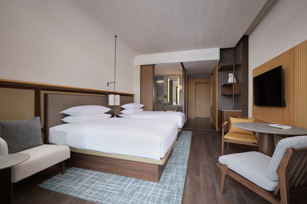A hotel room with a large bed, two bedside tables, a sofa, a chair, a small table, and a TV mounted on the wall.