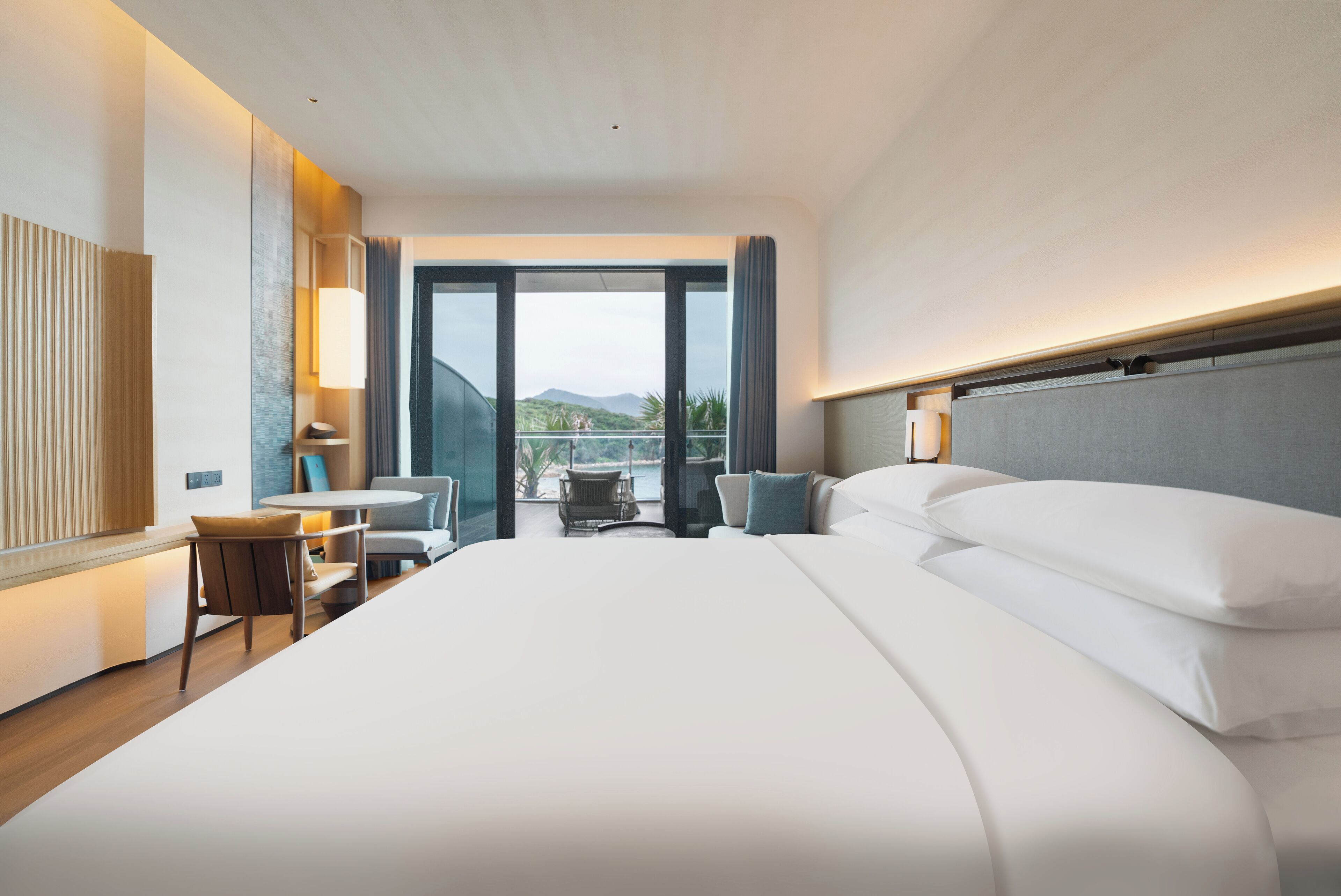 Una habitación de hotel moderna con una cama grande, un escritorio y un balcón con vistas a las montañas.