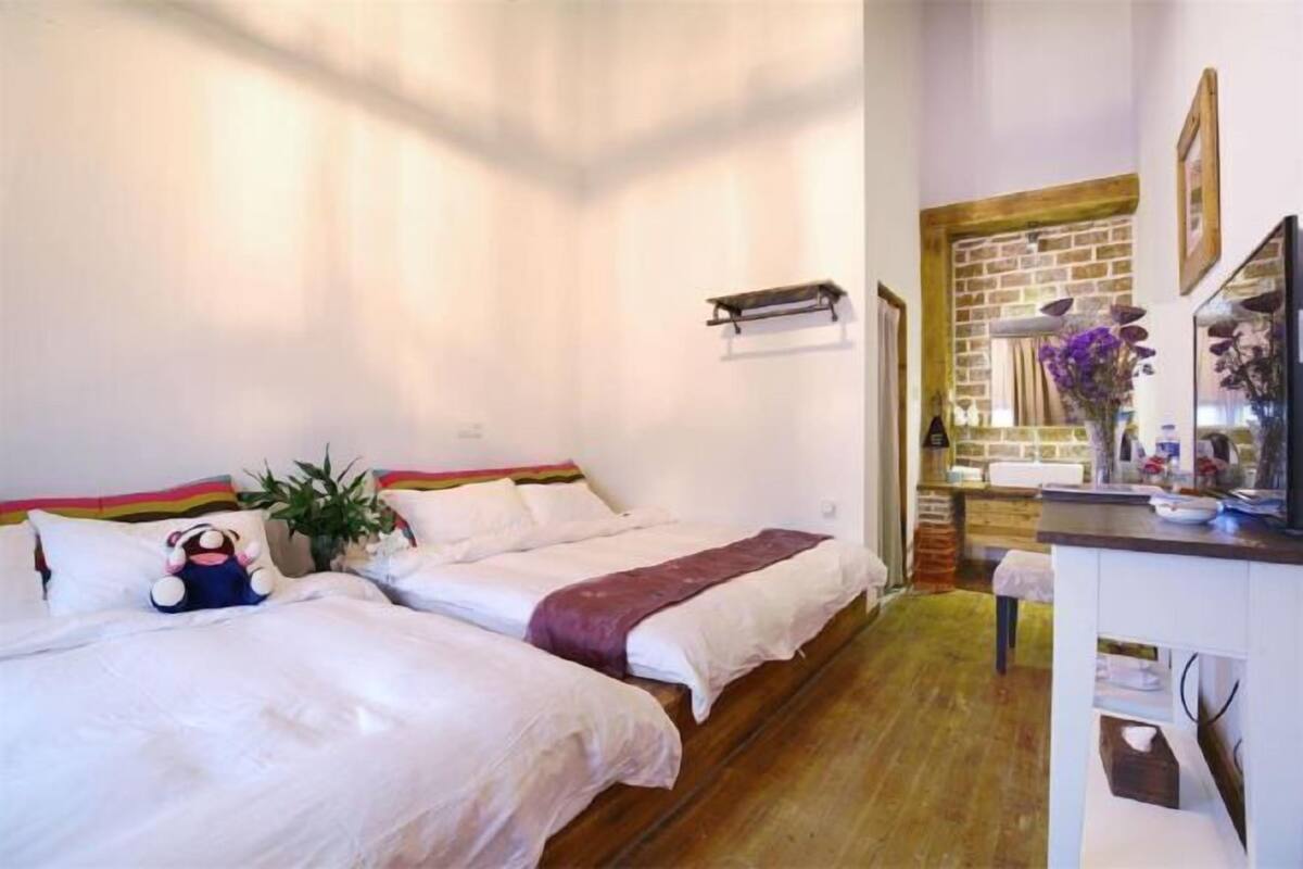 Una camera da letto con due letti, una piccola scrivania, un muro in mattoni e uno specchio.