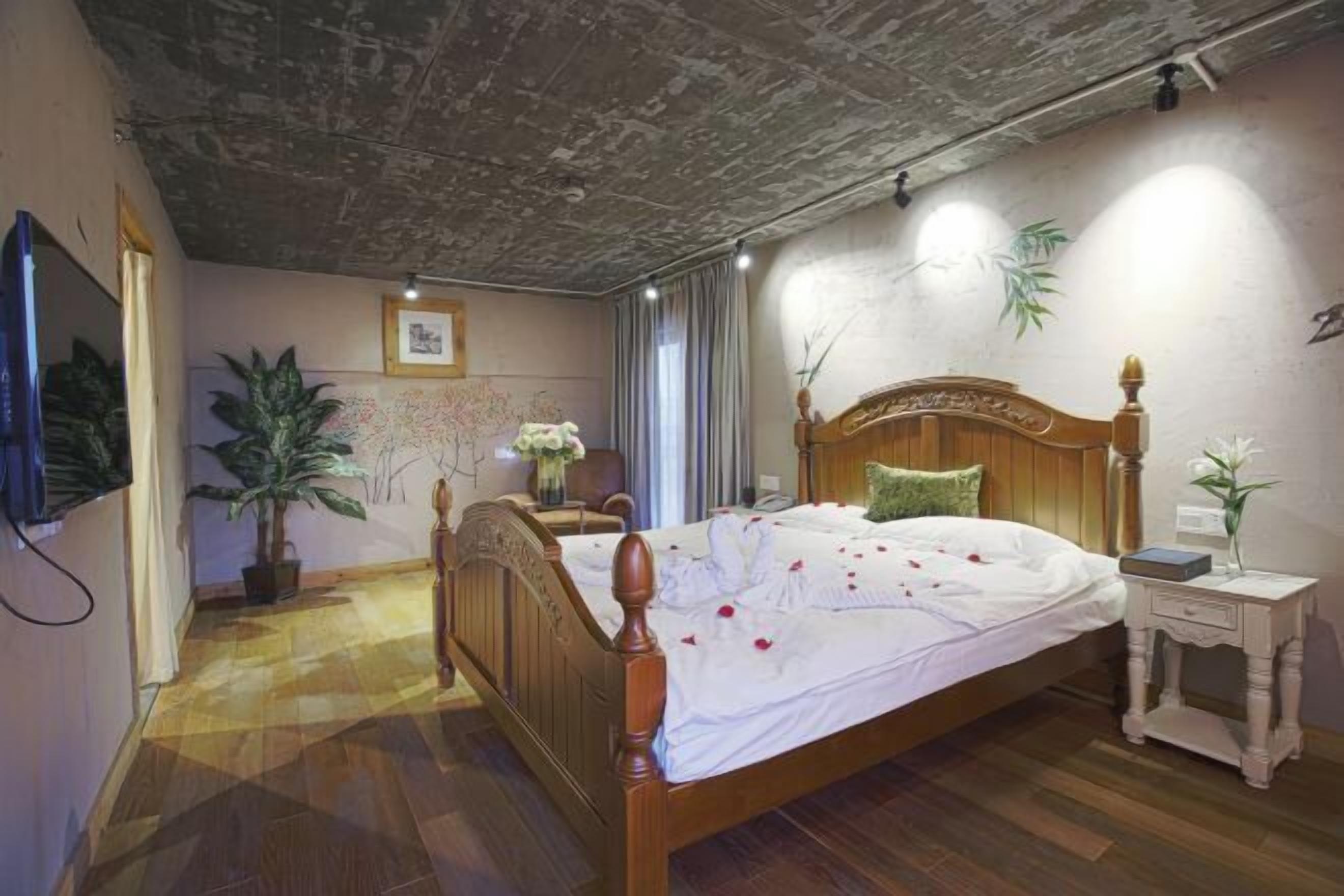 Une chambre à coucher avec un lit en bois, une table de chevet, un téléviseur fixé au mur et une grande plante en pot.