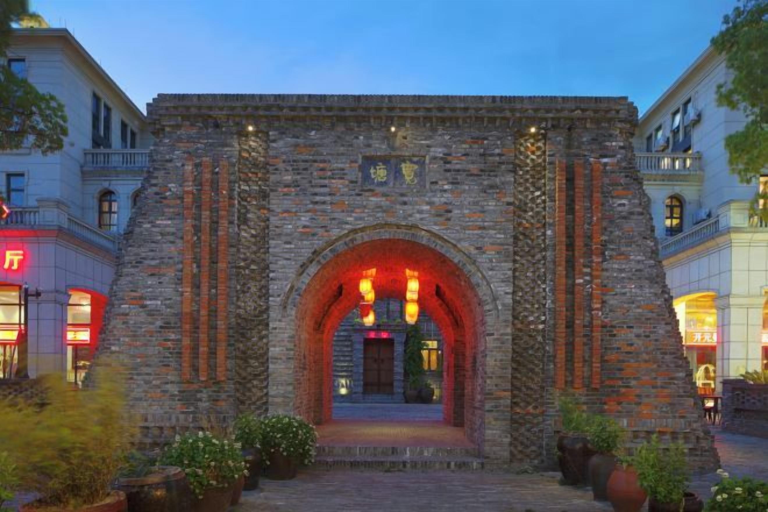 Une entrée en forme d’arc en pierre mène à un bâtiment, et un chemin pavé y conduit.