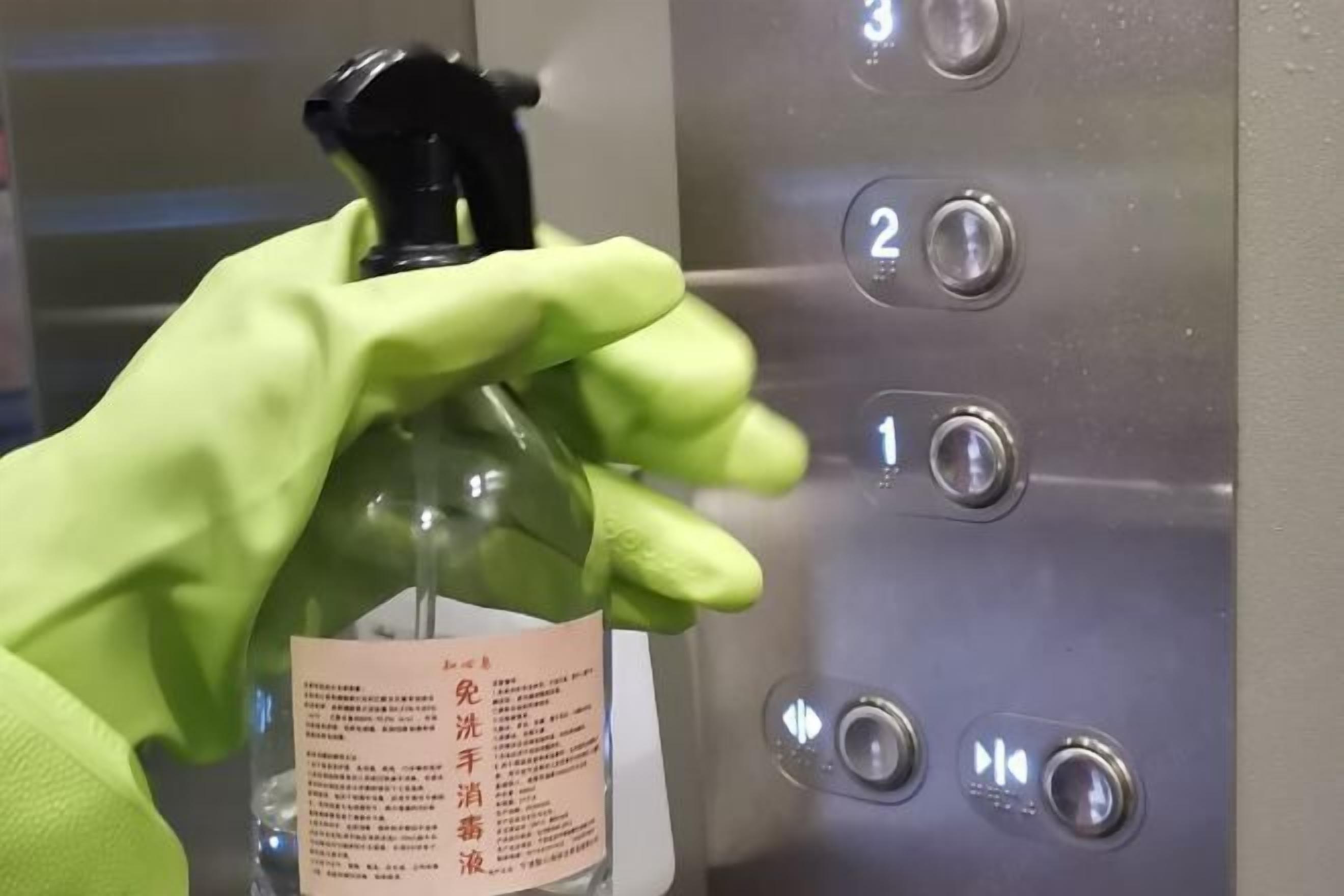Una mano sosteniendo un atomizador con una etiqueta, frente a un panel de control de ascensor con botones del 1 al 3.