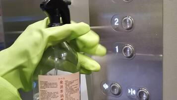 Una mano sosteniendo un atomizador con una etiqueta, frente a un panel de control de ascensor con botones del 1 al 3.