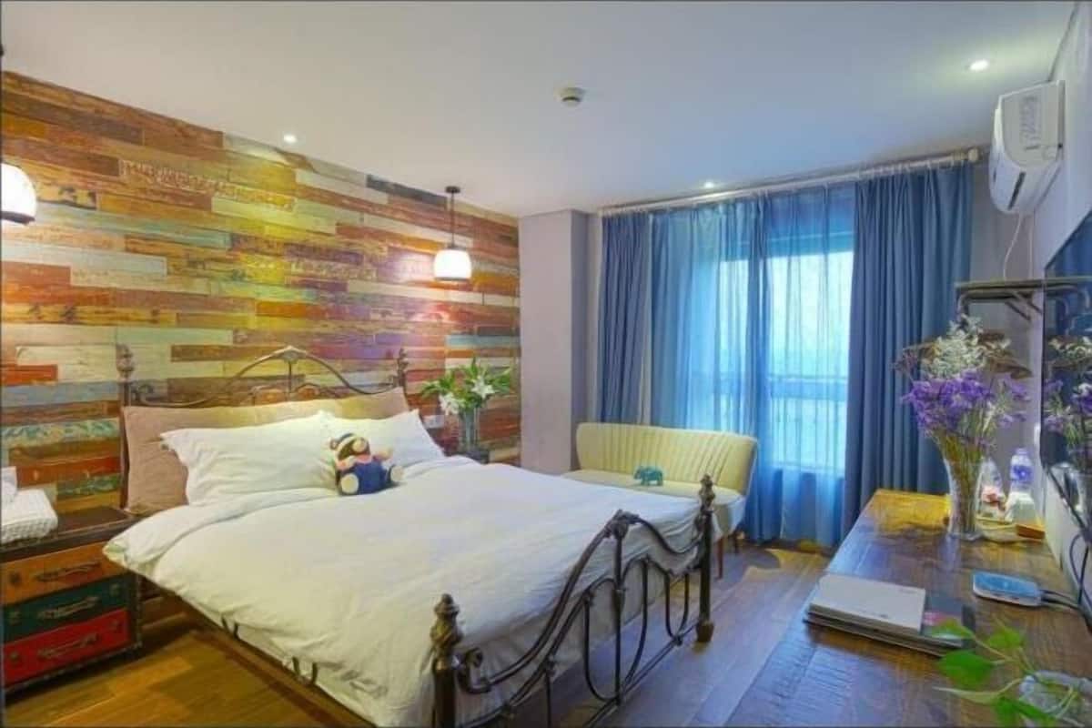 Una camera da letto con una testiera in legno, un letto con biancheria bianca, un comodino con una lampada e una finestra con tende azzurre.
