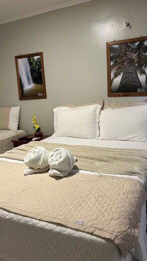 A hotel room with a bed, two pillows, a nightstand with a remote control, a potted plant, and two framed pictures on the wall. - Pousada Coco Babaçu (Vicosa do Ceara)