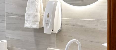 A bathroom with a sink, mirror, towel rack, toilet, and hand dryer.