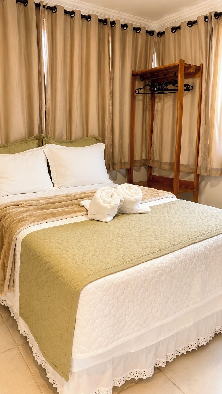 A neatly made bed with a green and white quilt, a wooden headboard, and a wooden chair with a coat rack.