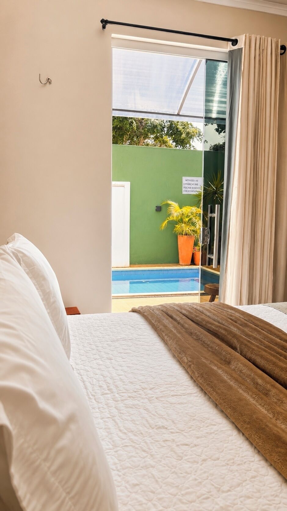 A hotel room with a bed, a view of a swimming pool, and a green wall.