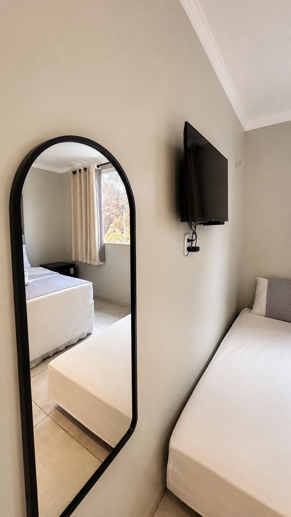 Une chambre à coucher avec un lit, un téléviseur fixé au mur et un miroir qui reflète la pièce.