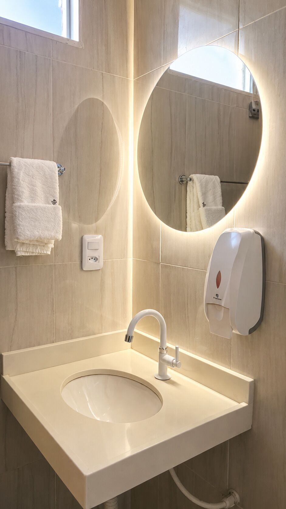A bathroom with a round mirror, a sink, a towel rack, and a soap dispenser.