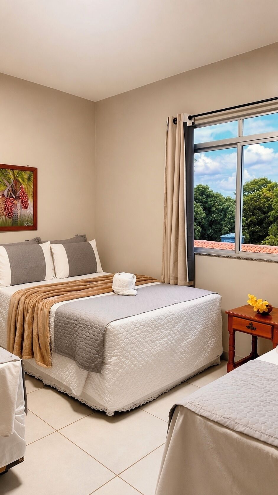 A hotel room with a bed, a small table, a chair, and a window with a view of trees.
