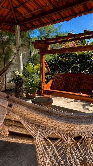 A hammock, wooden bench, and potted plants under a wooden pergola. - Pousada Coco Babaçu (Vicosa do Ceara)