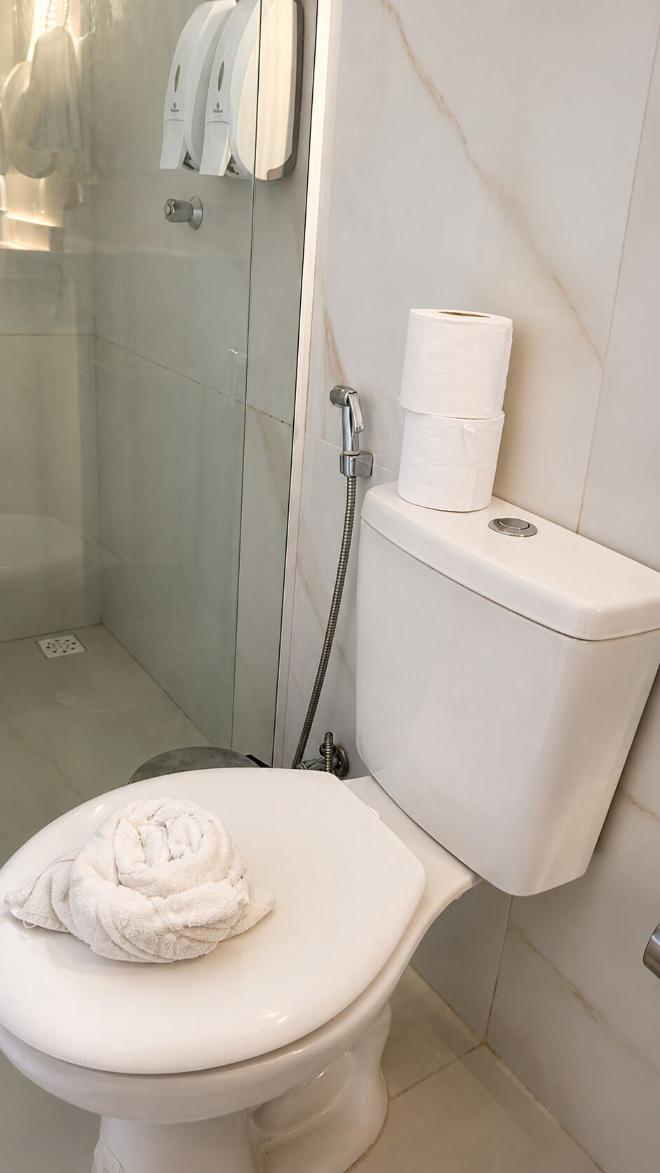A bathroom with a toilet, a shower, and a towel on the seat.