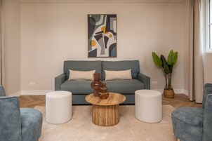 Un salon avec un canapé gris, deux poufs blancs, une table basse en bois et une plante en pot.