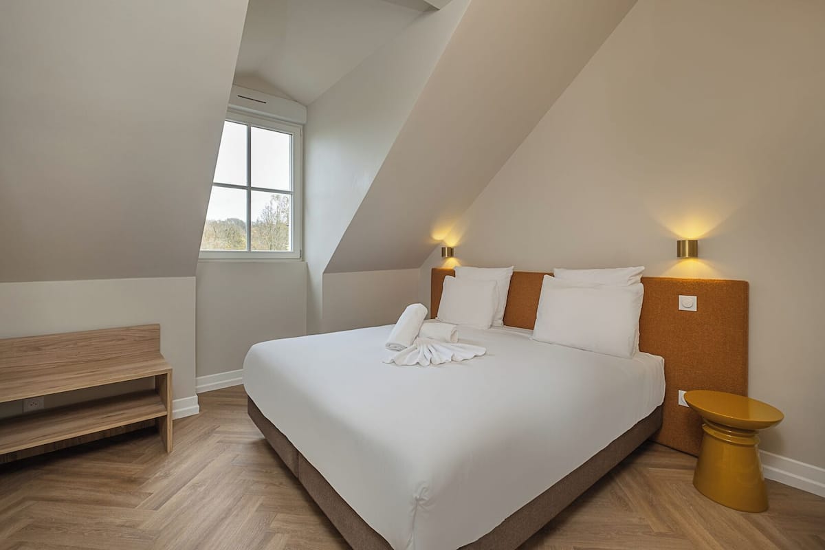 A bedroom with a large bed, a bench, a small table, and a window.