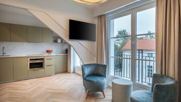 A modern living room with a large window, a flat-screen TV mounted on the wall, and a grey armchair.