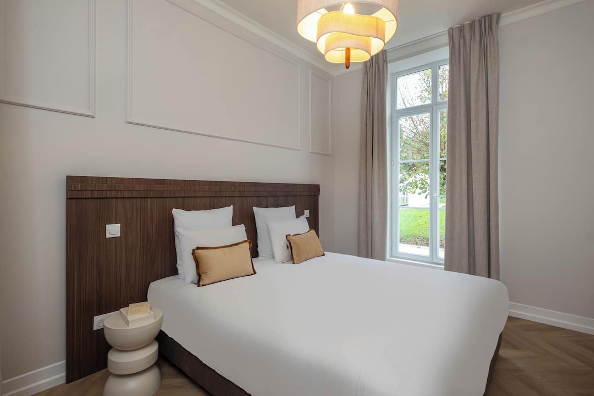 A neatly arranged bedroom with a large bed, a bedside table, and a window with curtains.