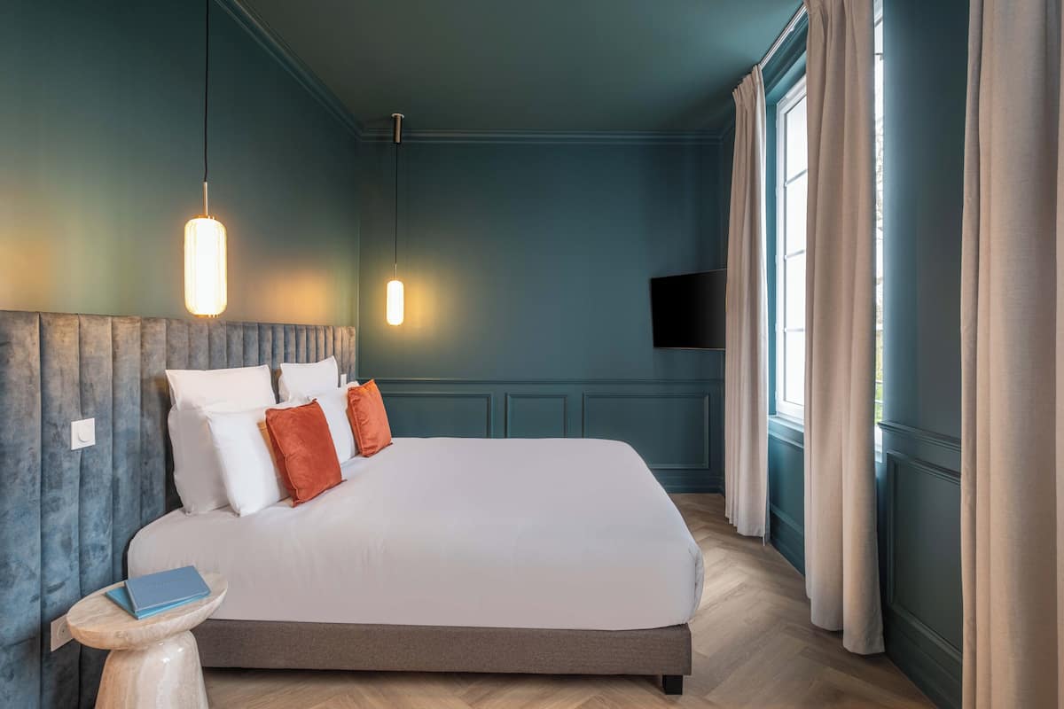 A bedroom with a large bed, two bedside lamps, a small table with a book, and a TV mounted on the wall.