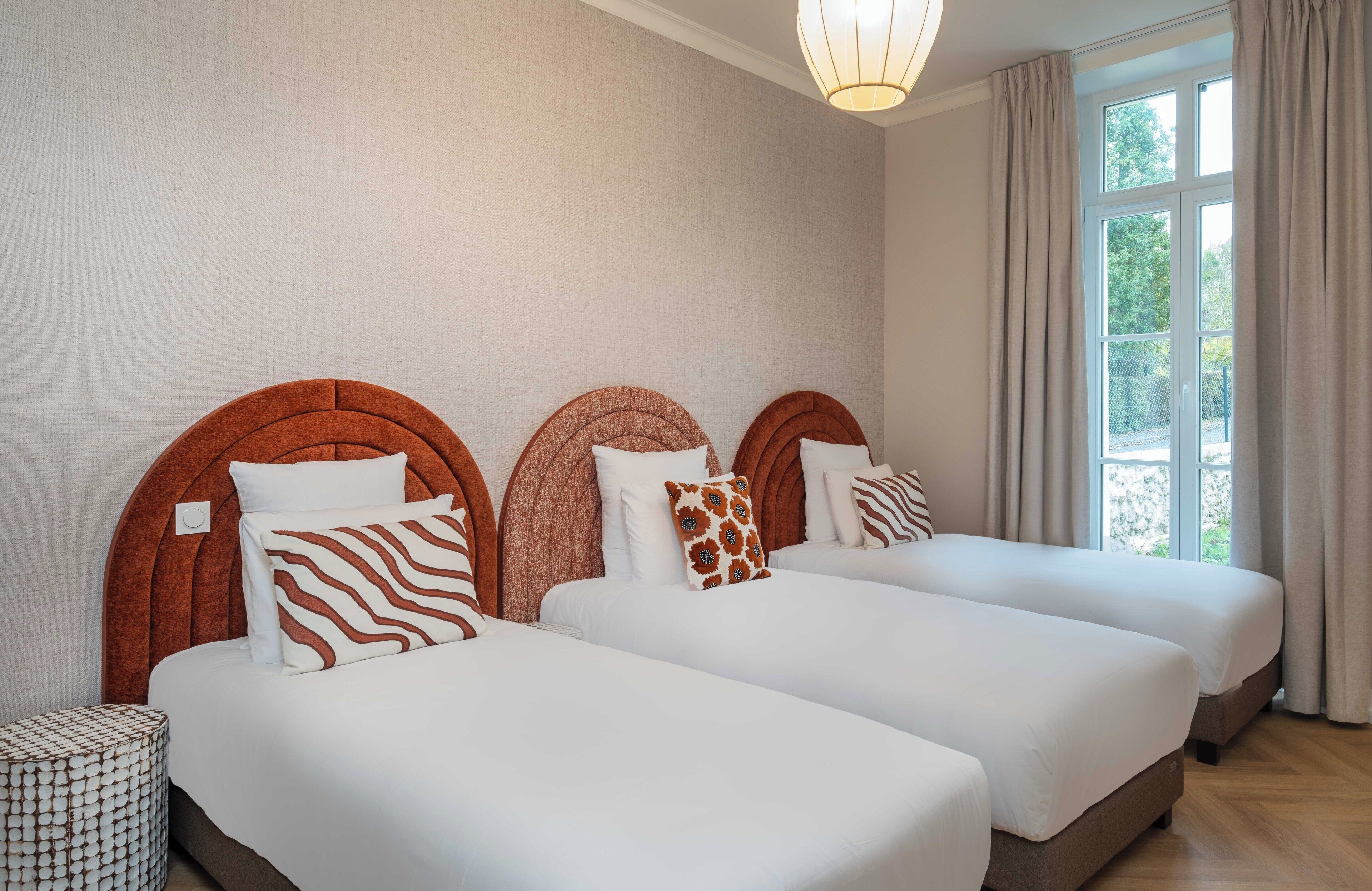 A hotel room with three beds, each with a unique headboard design, white bedding, and a small side table.