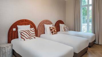 A hotel room with three beds, each with a unique headboard design, white bedding, and a small side table.