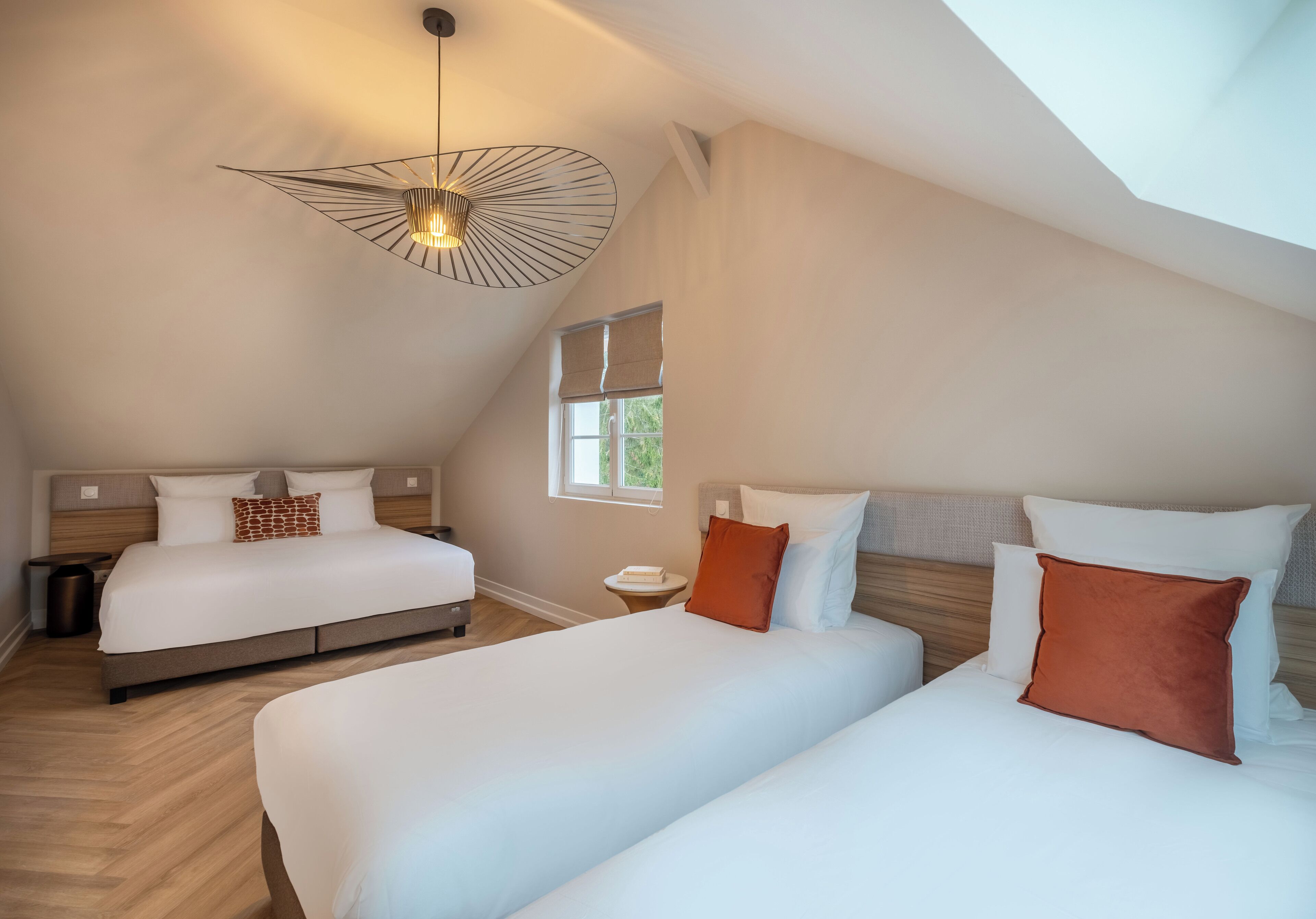 A modern hotel room with two beds, a skylight, and a large window.