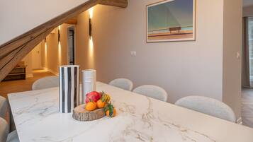 A modern dining area with a marble table, fruit centerpiece, and a painting on the wall.