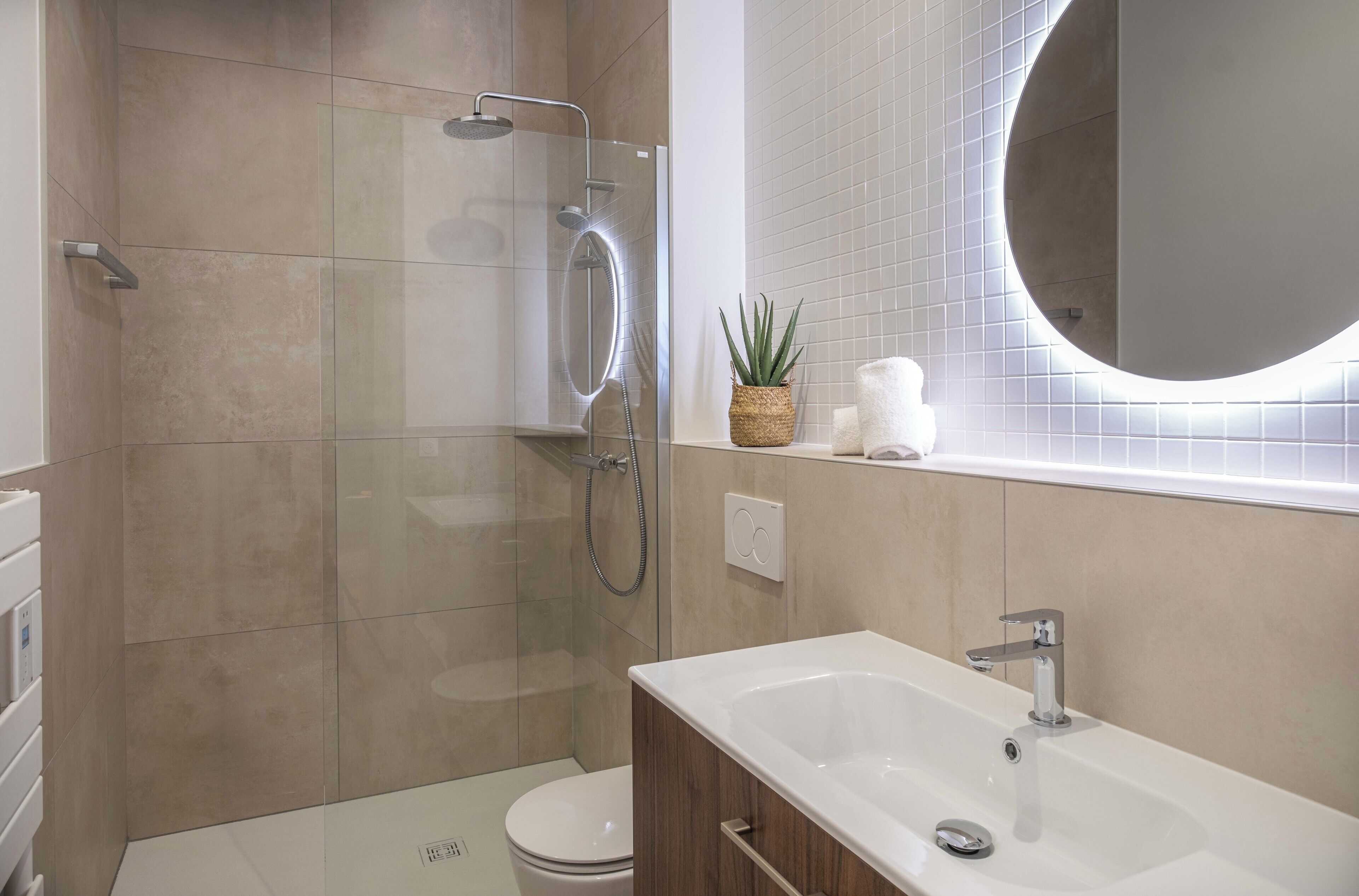 A modern bathroom with a glass-enclosed shower, a freestanding bathtub, and a round mirror above the sink.