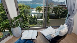 Una habitación moderna con un ventanal grande que ofrece vistas a un paisaje costero, un rincón con asientos acolchados y una planta en maceta.