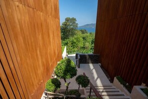 A view through a wooden structure with a pathway leading to a seating area and a view of greenery and a distant landscape. - New 2Br Condo Bluepoint 8-17 Sea Views (Phuket)