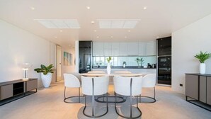 Una cocina moderna con armarios blancos, una isla central y un comedor con cuatro sillas blancas.