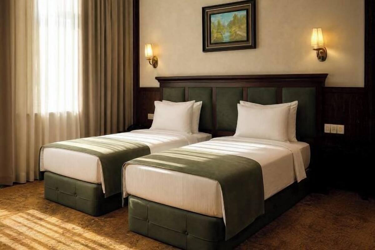 A hotel room with two beds, a painting on the wall, and two wall-mounted lamps.