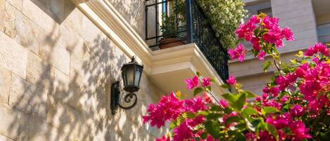 A building facade with a stone wall, a black wrought iron balcony, and vibrant pink bougainvillea flowers.