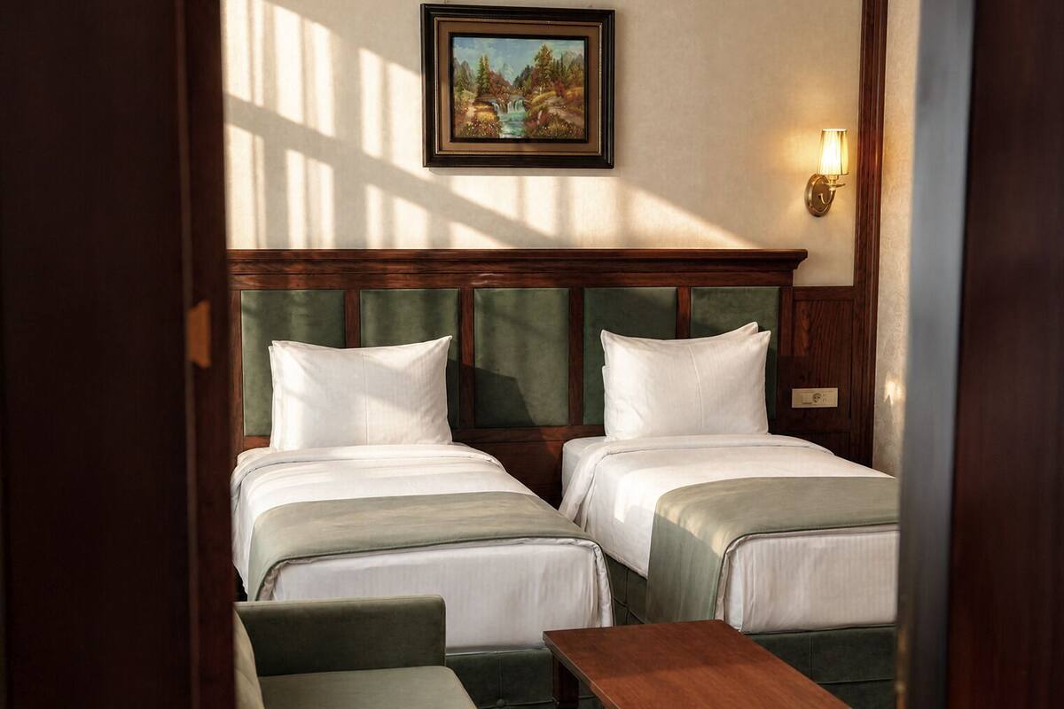 A hotel room with two beds, a wooden headboard, a painting, a nightstand, and a small table.