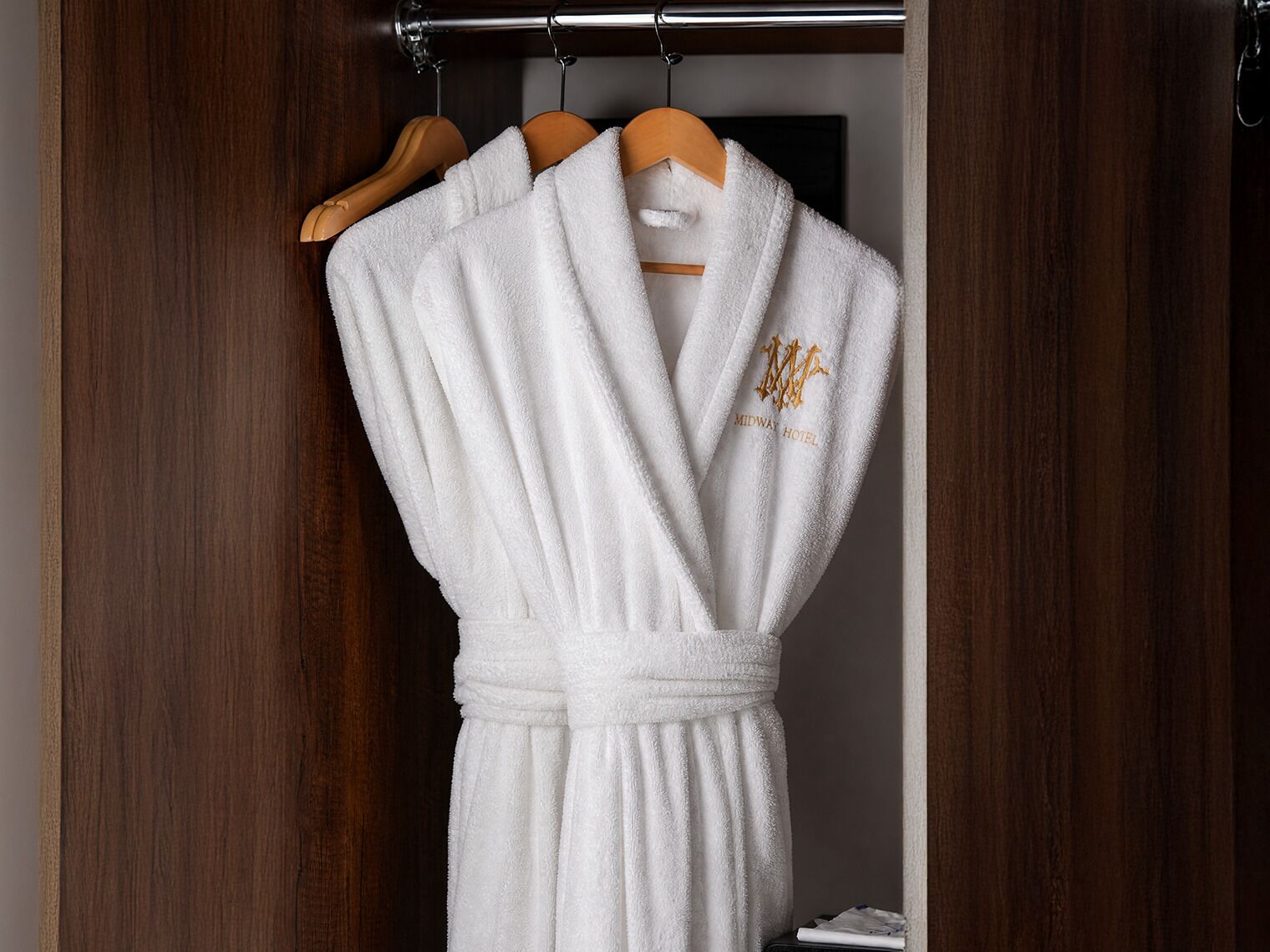 Een witte badjas met een gouden embleem, opgehangen aan een houten kleerhanger.