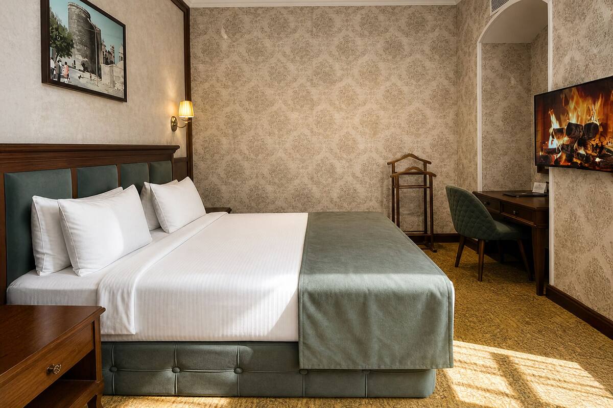 A hotel room with a large bed, a desk, a chair, and a television.