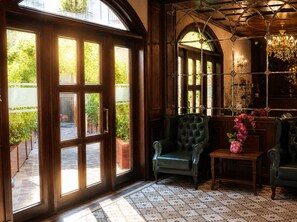 A room with a large arched window, a green upholstered chair, a small table with a vase, and a chandelier. - Midway Baku Hotel (Baku)
