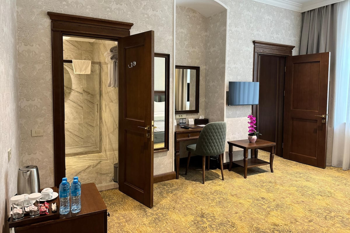 A hotel room with a marble bathroom, a desk with a chair, a TV, and a small table with a vase.