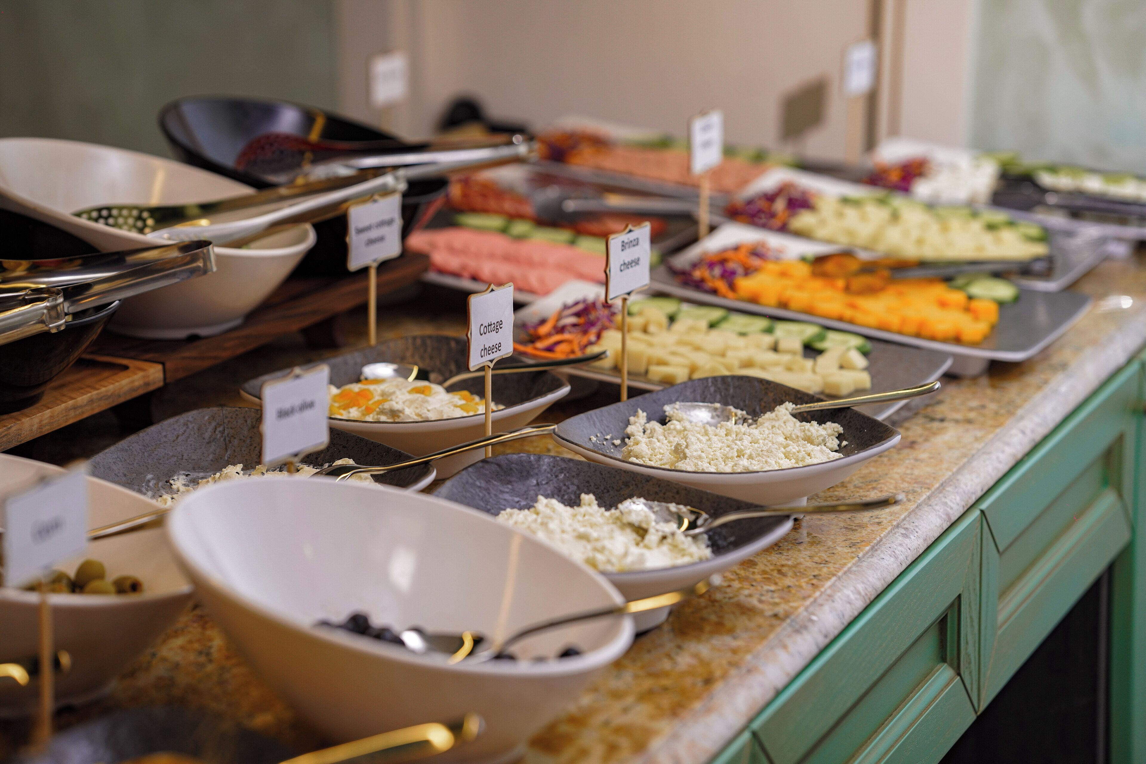 A buffet with various dishes labeled, including cottage cheese, brie cheese, and other items.
