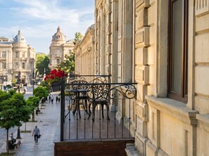 Un balcón con baranda de hierro forjado, una mesa y sillas, con vistas a una calle de la ciudad con edificios históricos.