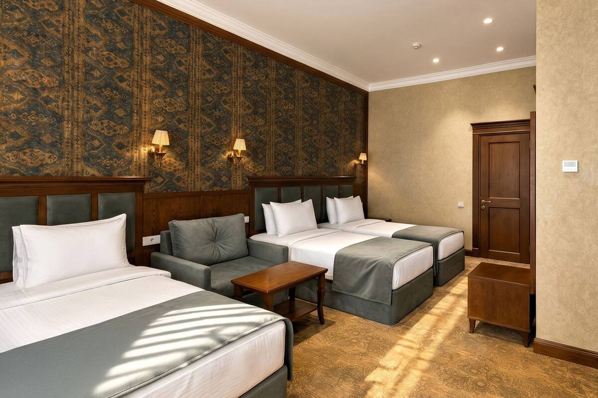 A hotel room with three beds, a sofa, a wooden cabinet, and patterned wallpaper.