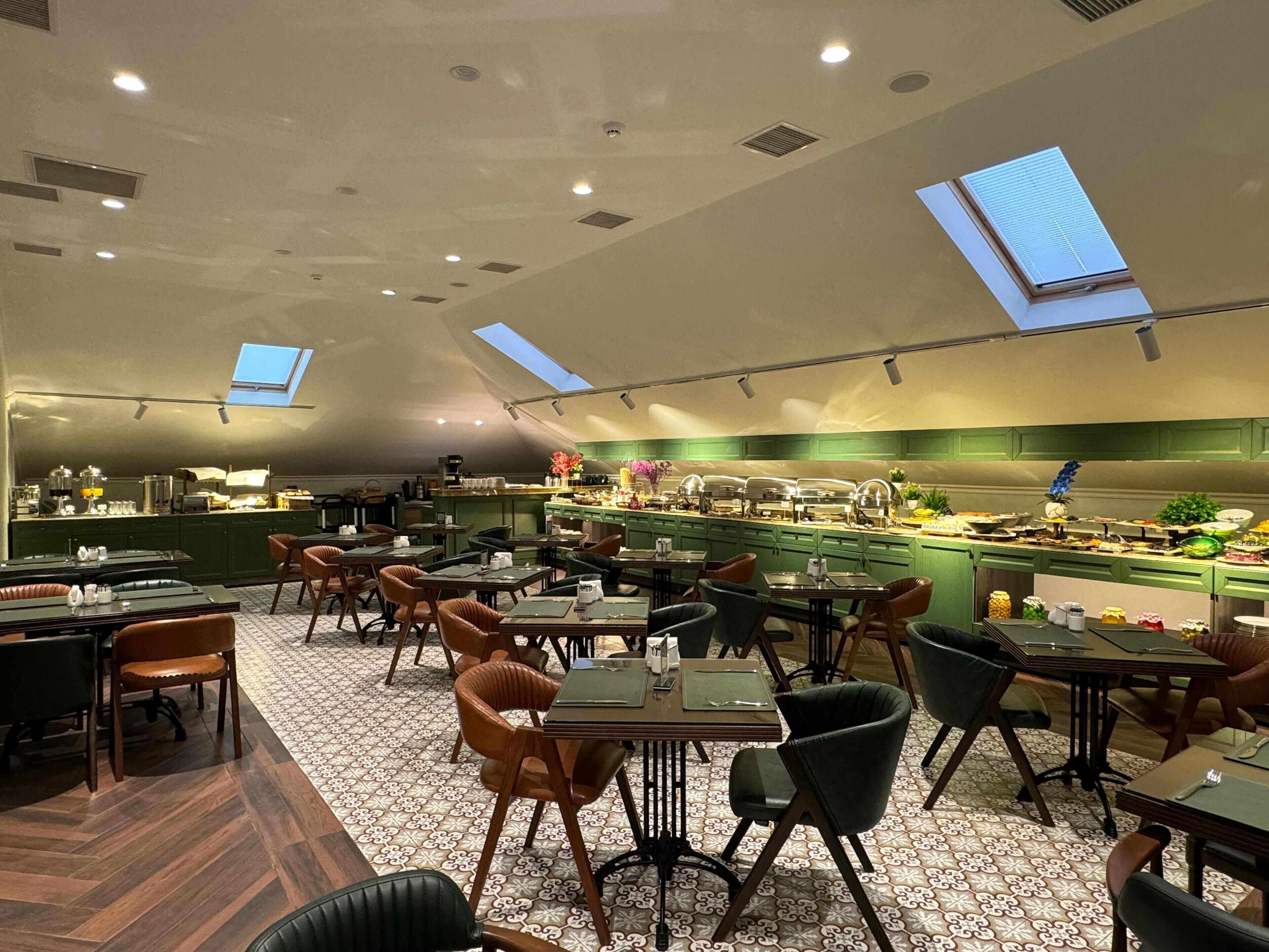 A restaurant with a high ceiling, skylights, and a buffet area.