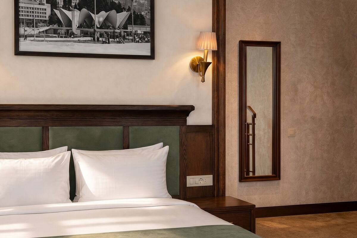 A hotel room with a bed, a nightstand, a wall-mounted lamp, a framed picture, and a mirror.
