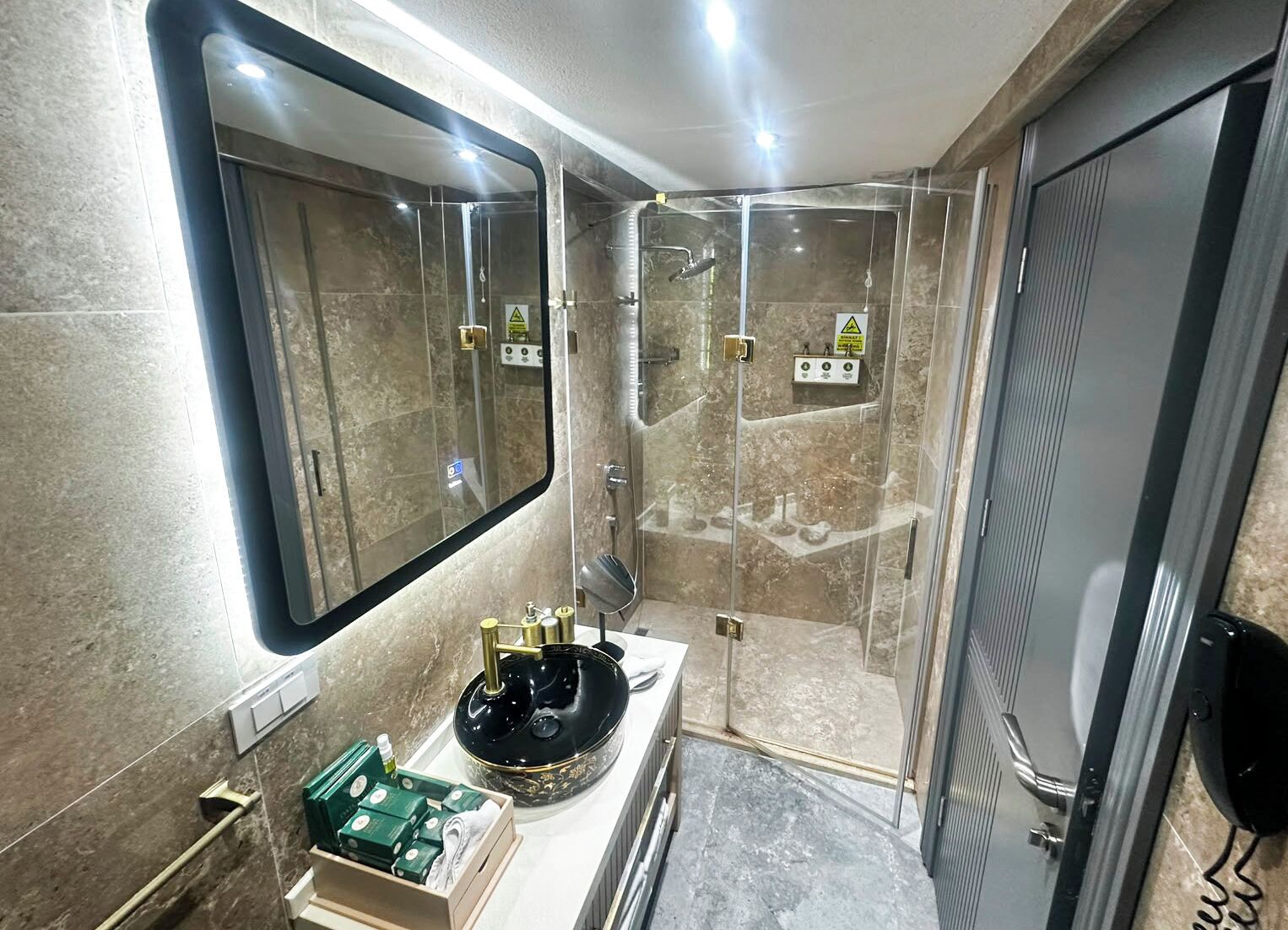 Un baño moderno con ducha de vidrio, tocador con lavabo negro y espejo sobre el lavamanos.